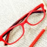 red glasses on a book with pencil